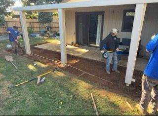 Workers measuring and marking a patio area beside a house for construction or landscaping
