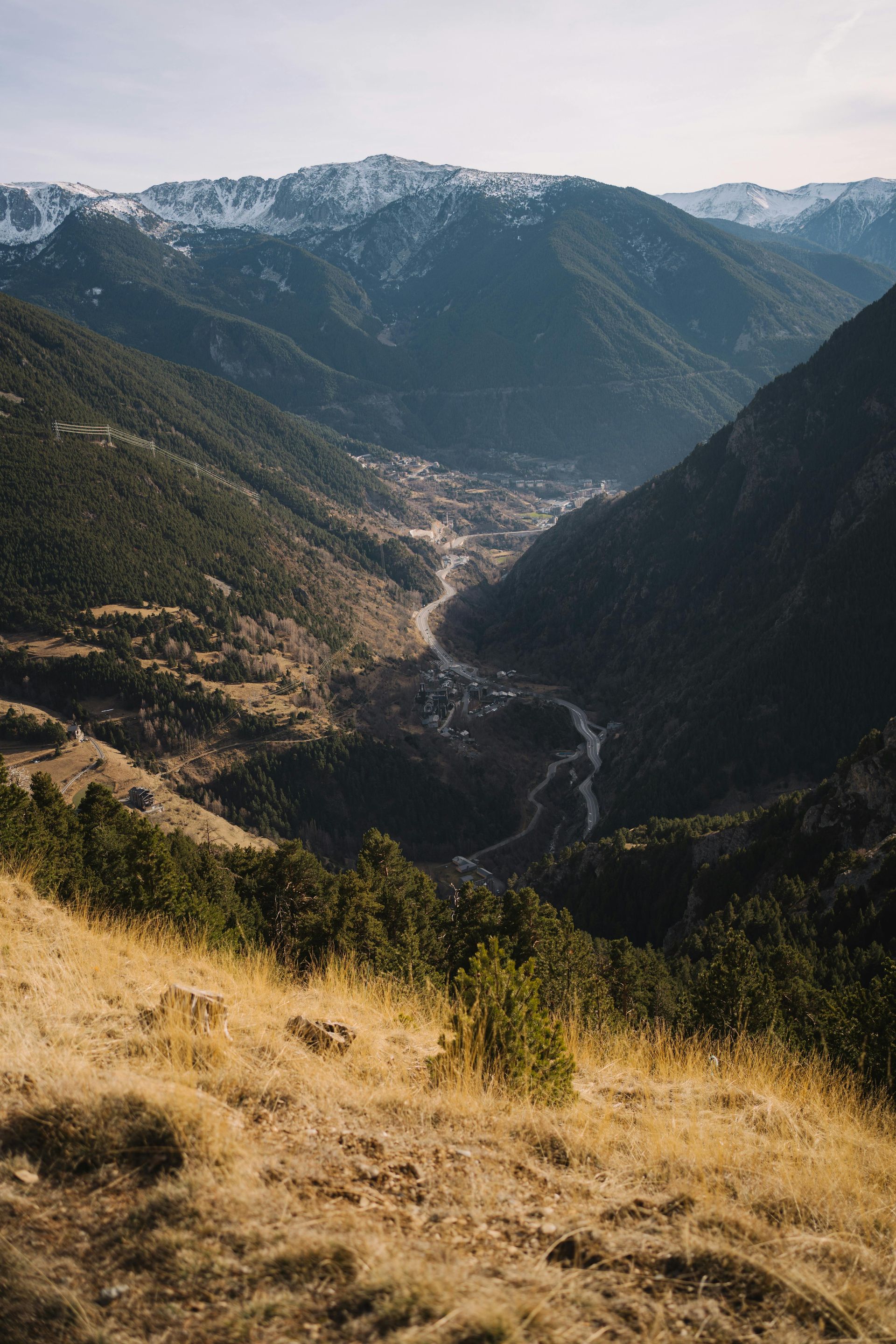 Valle de montaña con río sinuoso, pueblo enclavado entre laderas verdes, picos nevados bajo un cielo azul. montaña de andorra