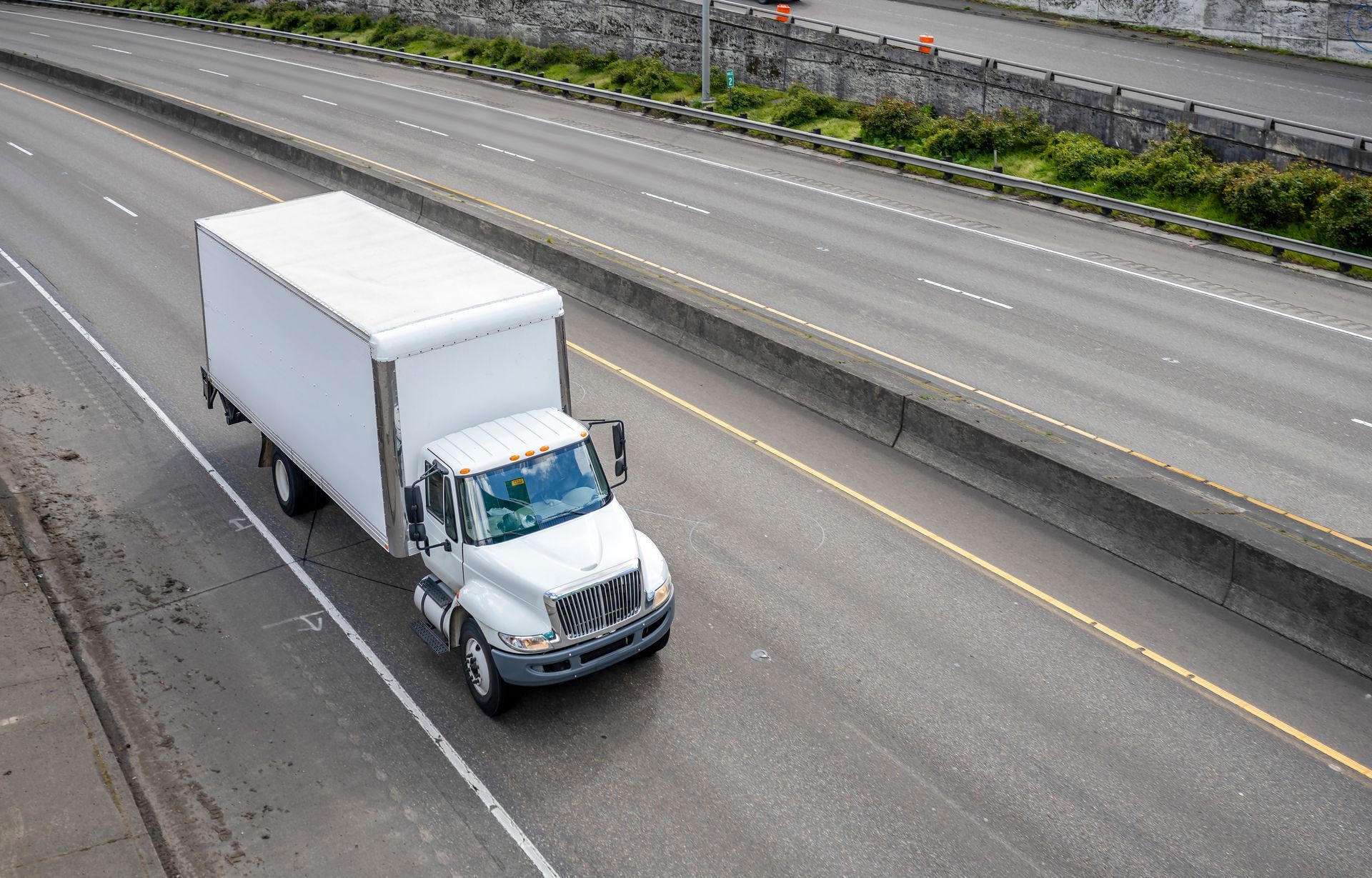 A white box moving truck driving on a multi-lane interstate highway.
