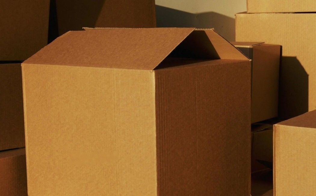 Brown cardboard moving boxes stacked in warm indoor light, one box open at the top. Brown cardboard moving boxes stacked in warm indoor light, one box open at the top.