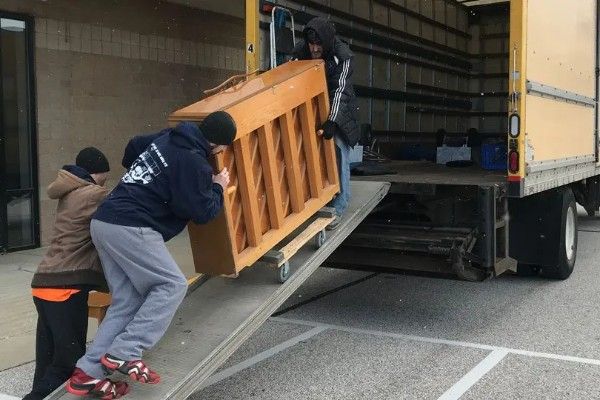 Workers loading a piano up a ramp into a truck at a warehouse loading dock Workers loading a piano up a ramp into a truck at a warehouse loading dock