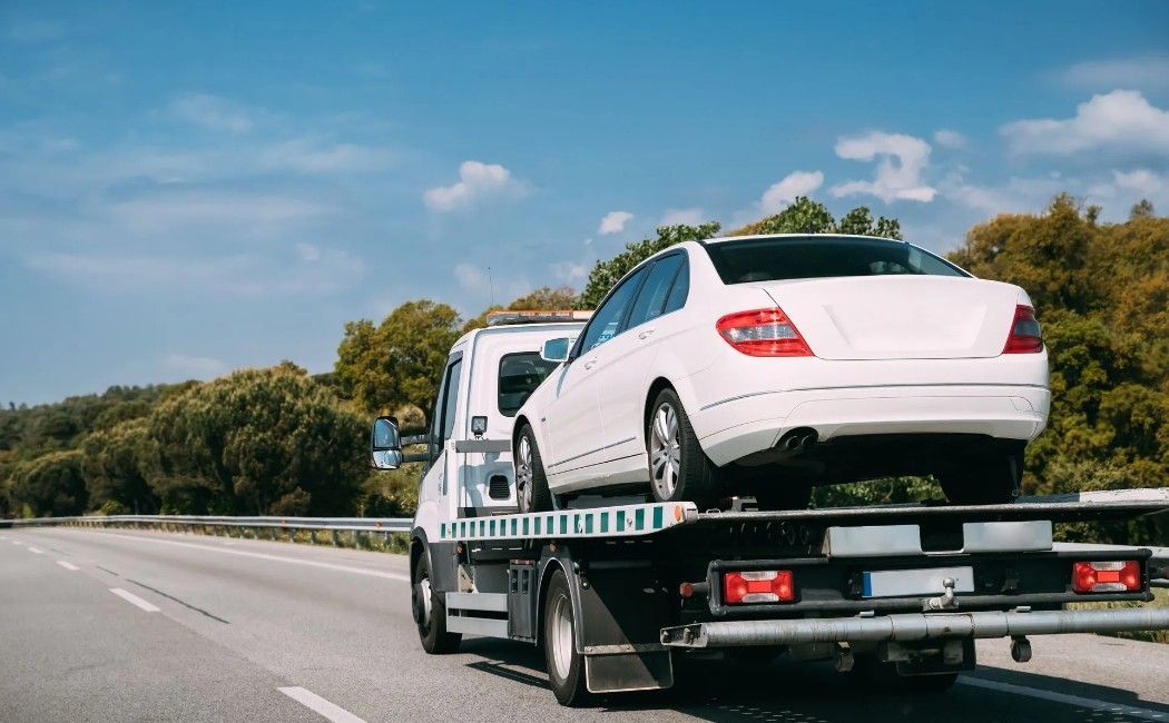 White sedan secured on a car carrier truck driving on a highway White sedan secured on a car carrier truck driving on a highway