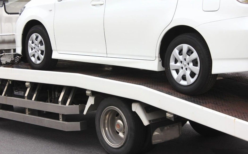 White sedan loaded on a car carrier tow truck