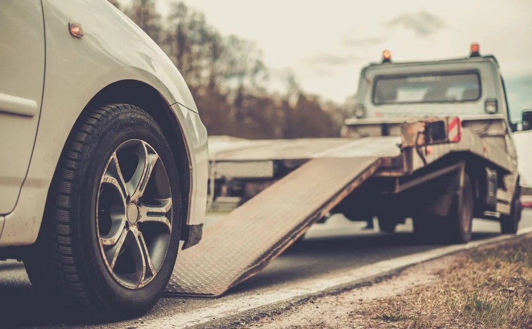 Tow truck loading a white car onto a flatbed on a road