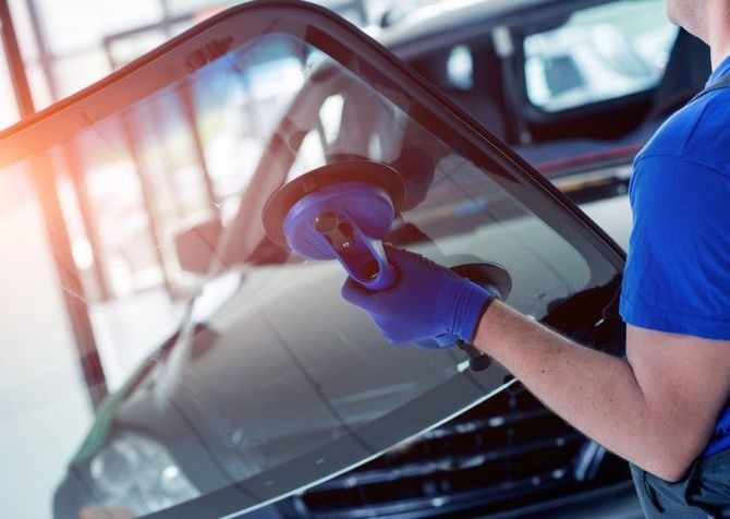 Technician polishing a car windshield in a repair shop, wearing blue gloves and shirt