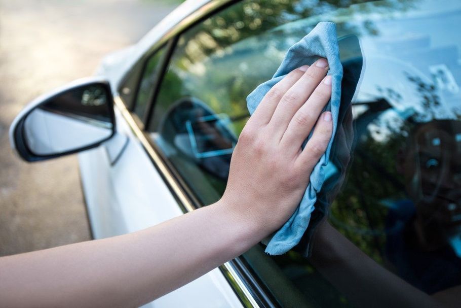 Hand wiping a car window with a blue cloth near the side mirror