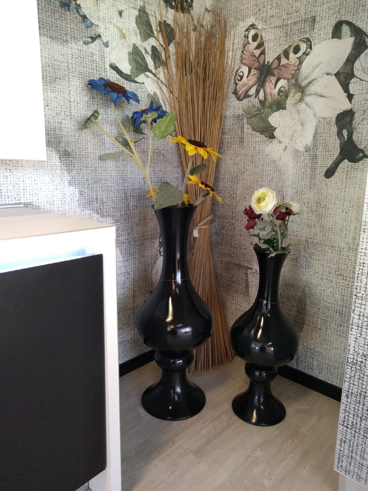 Due vasi neri con fiori vicino alla carta da parati a motivi.