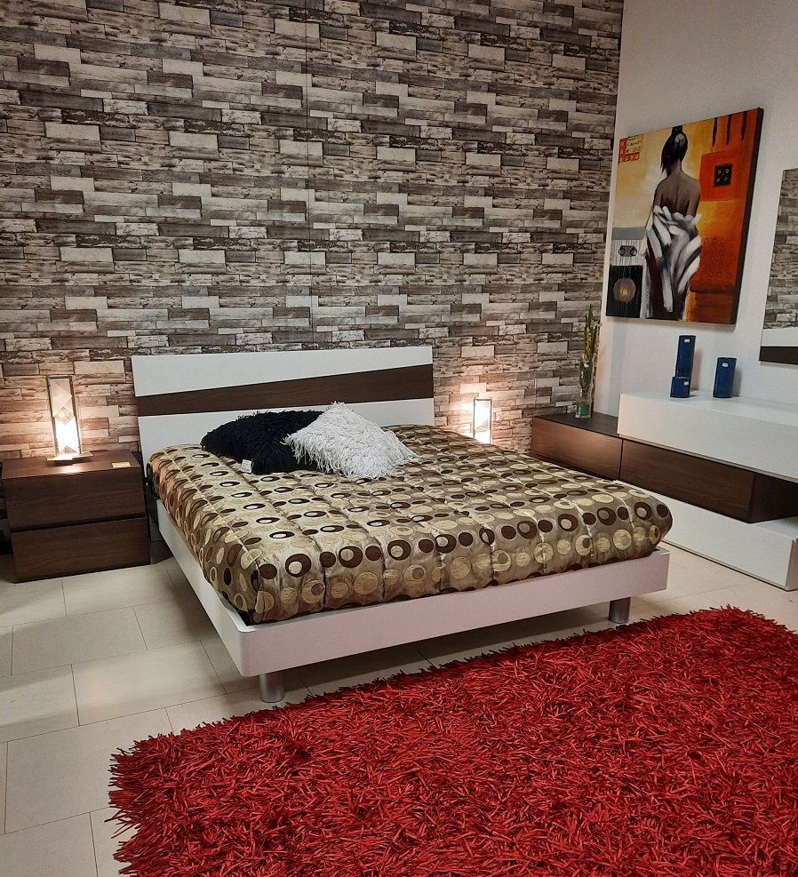 Camera da letto con letto, tappeto rosso e opere d'arte su una parete di mattoni.