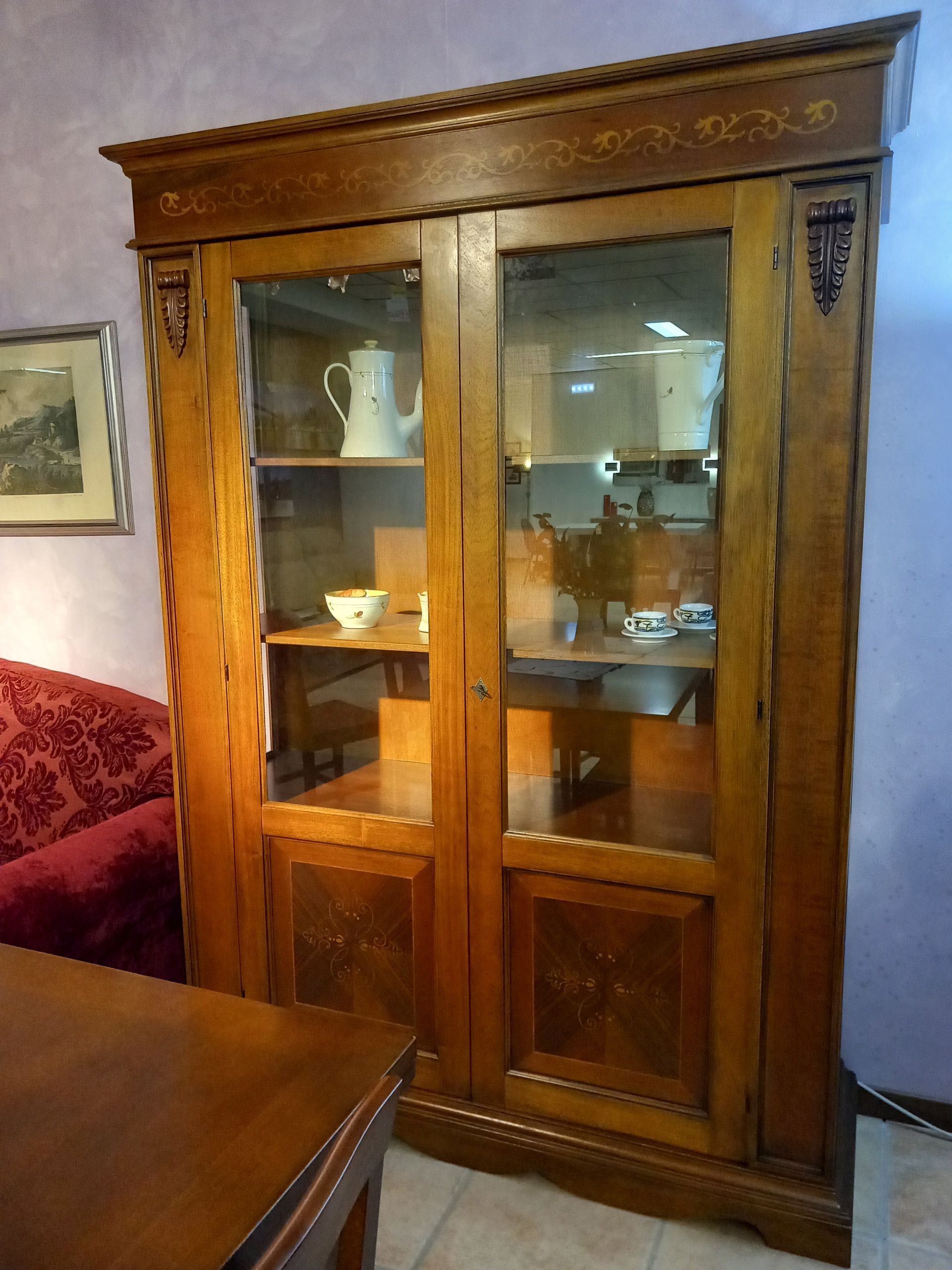 Vetrina in legno con ante in vetro, contenente stoviglie, posizionata in una stanza.