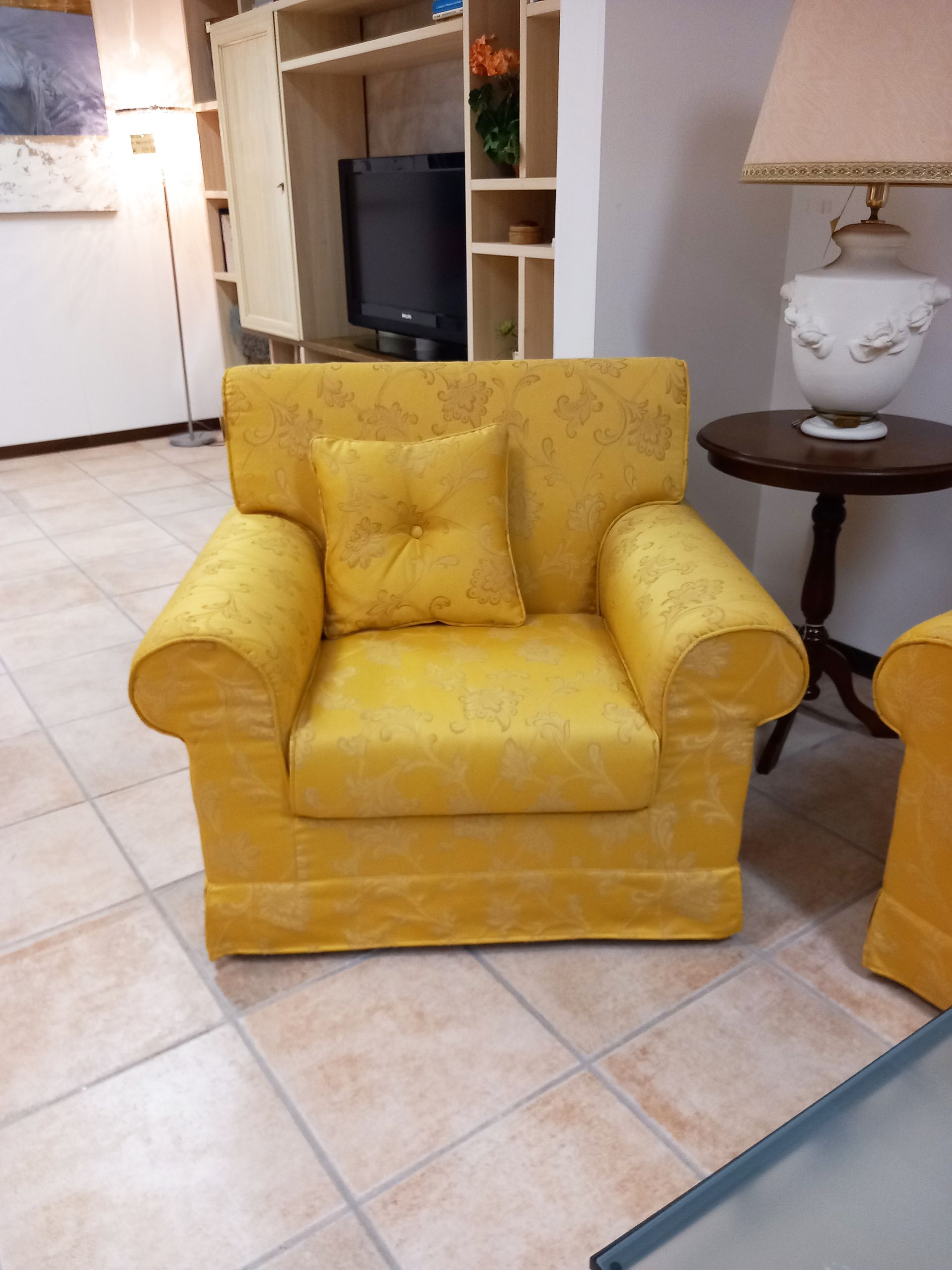 Poltrona gialla con cuscino coordinato, posizionata in un soggiorno con tavolino laterale e scaffalature integrate.