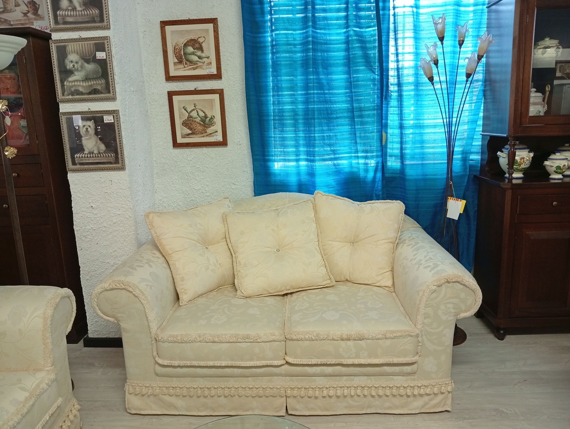 Divano beige con tre cuscini quadrati, in una stanza con tende blu e mobili antichi.