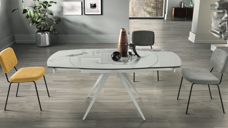 Tavolo da pranzo bianco con piano in vetro estensibile, due sedie e oggetti decorativi.