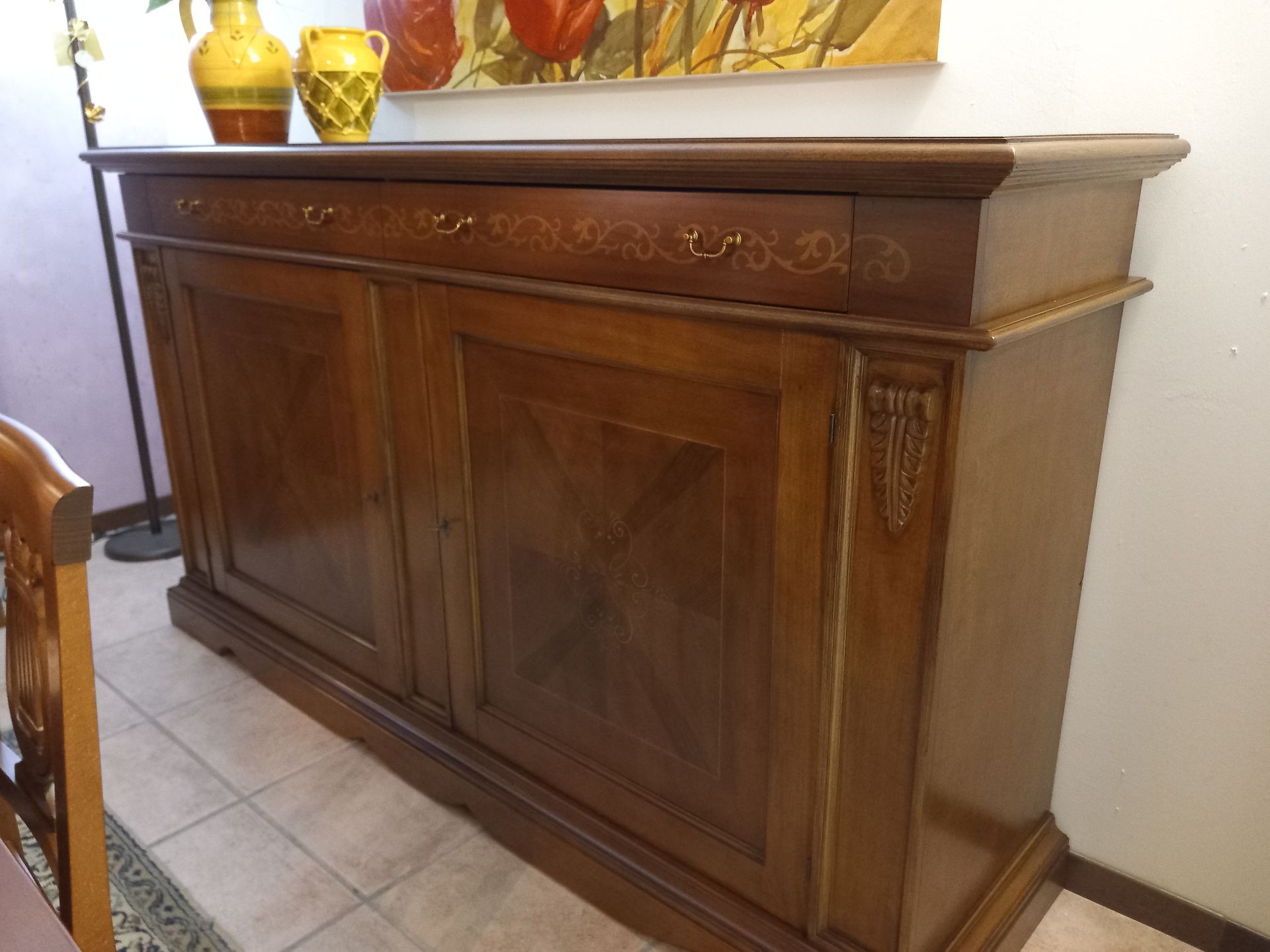 Credenza in legno con tre cassetti e due ante, vasi sopra, vicino a una parete.