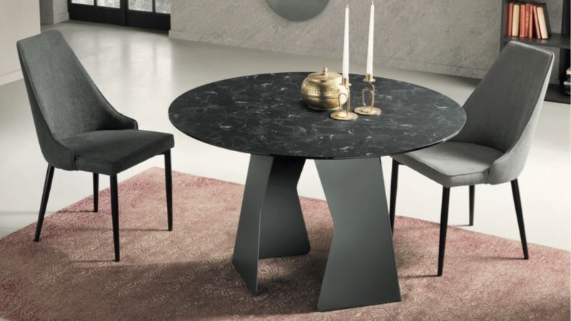 Un tavolo da pranzo rotondo in marmo nero con due sedie grigie, appoggiato su un tappeto rosa.