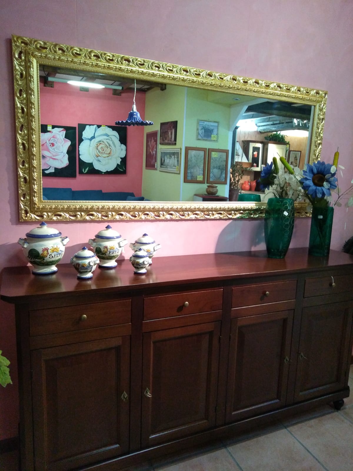 Grande specchio con cornice dorata decorata sopra una credenza in legno, decorata con vasi e porcellane.