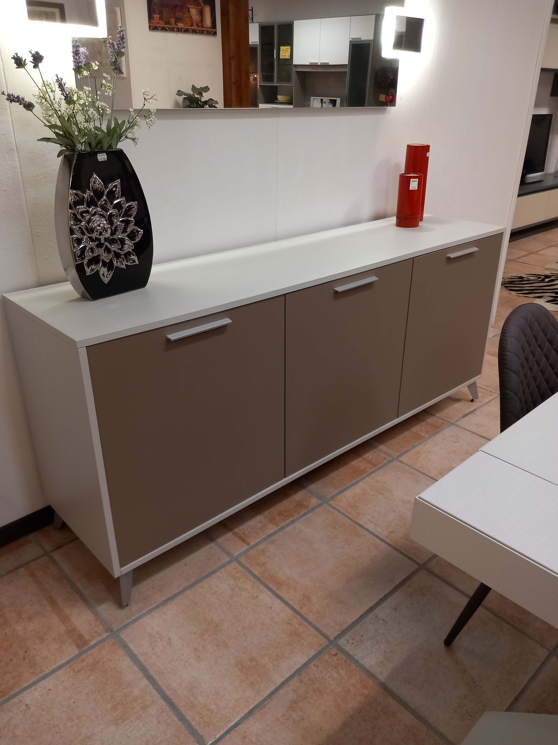 Mobiletto bianco e tortora con tre ante, maniglie argentate e un vaso sopra.