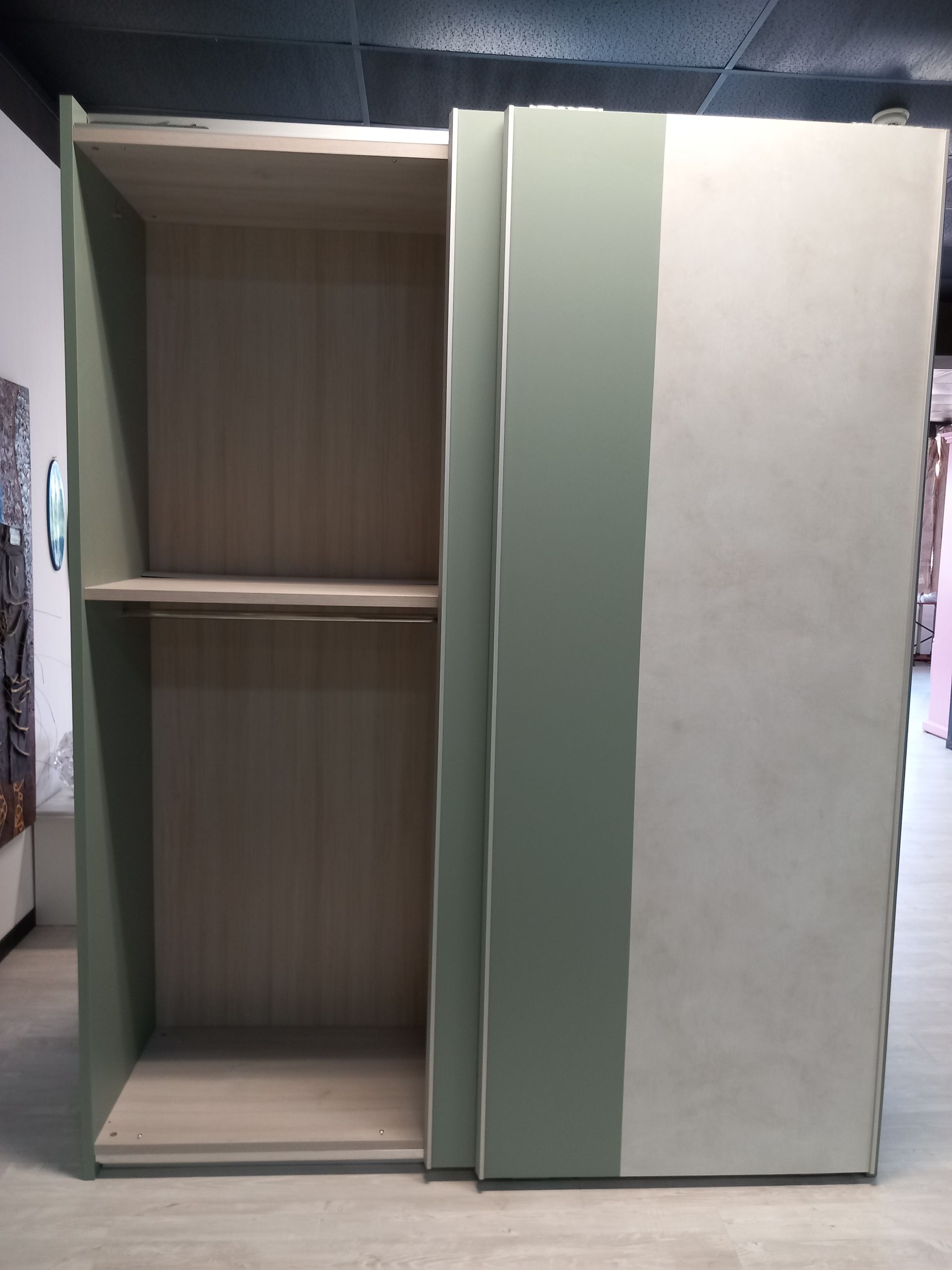 Armadio aperto con ante scorrevoli color verde e crema, ripiano interno e spazio aperto, su pavimento in legno.