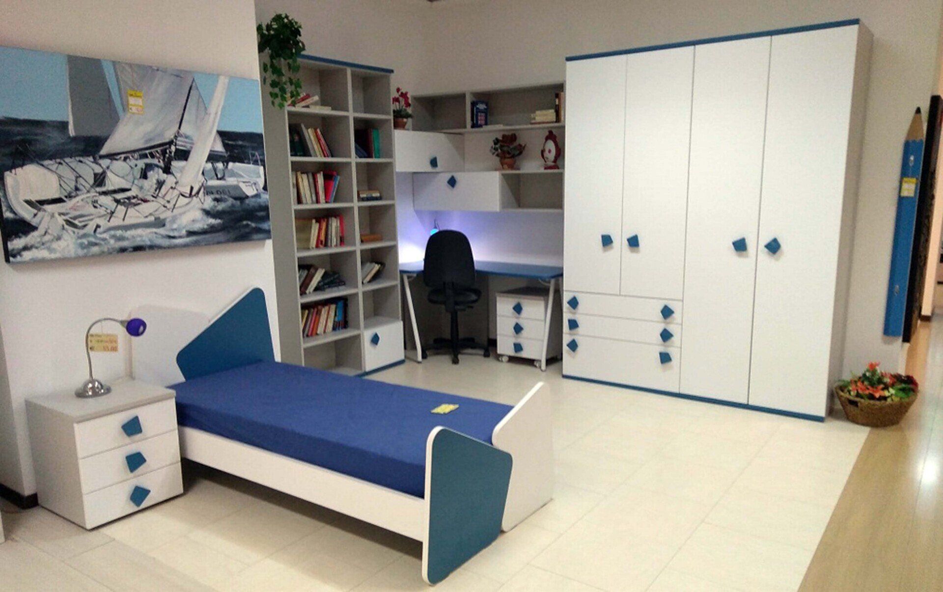 Set da camera da letto: mobili bianchi con dettagli blu, tra cui letto, armadio, scrivania, libreria e opere d'arte.