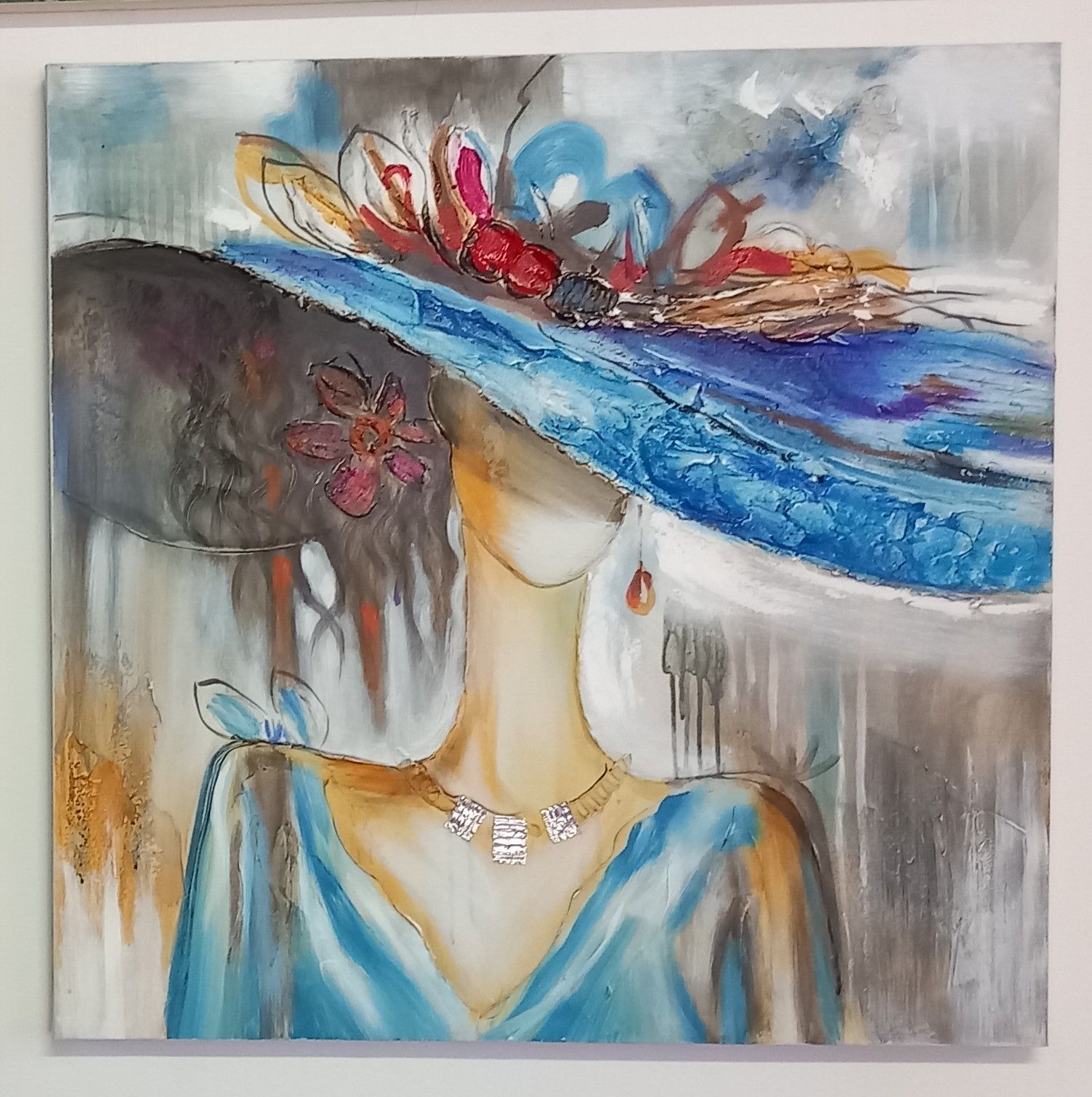 Donna che indossa un grande cappello blu con decorazioni floreali, un vestito blu e una collana.
