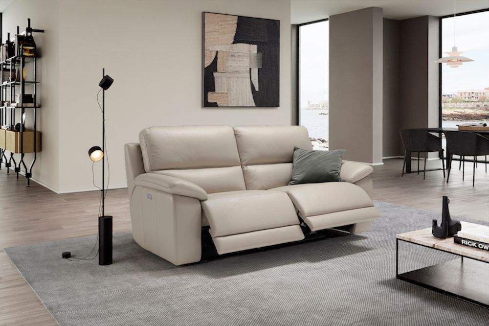 Divano reclinabile in pelle beige in un soggiorno moderno con tappeto grigio, opere d'arte e vista sull'oceano.