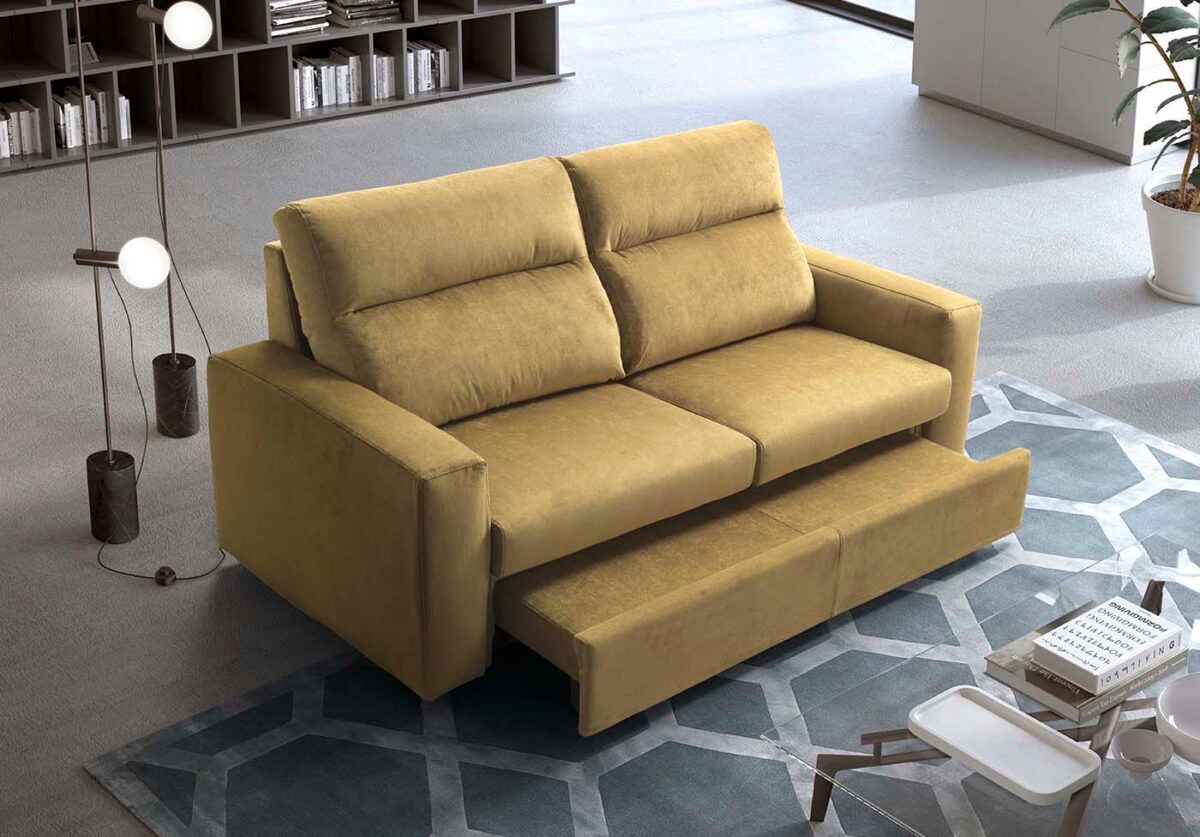 Divano letto giallo su un tappeto blu, con un tavolino da caffè e librerie sullo sfondo.