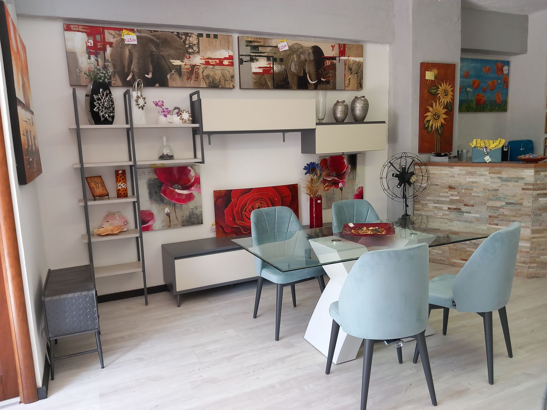 Esposizione di mobili con set da pranzo, scaffalature, quadri da parete e decorazioni.