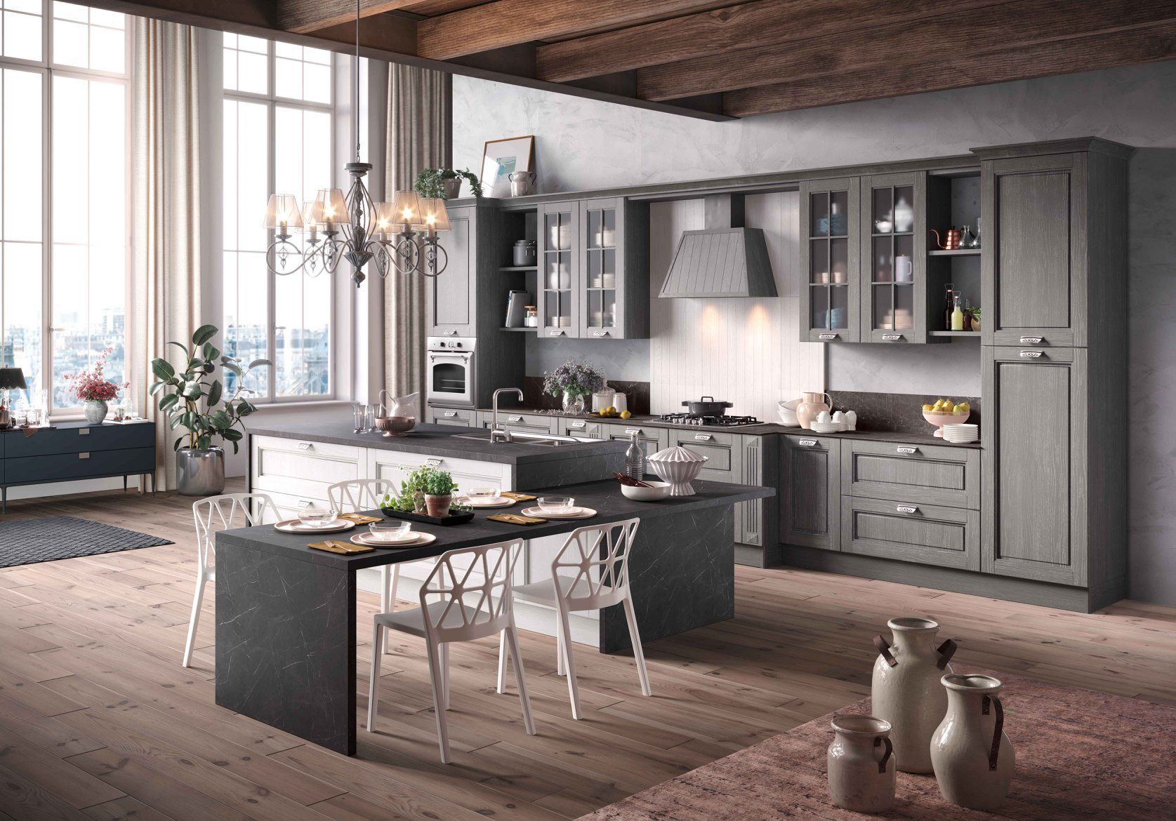 Ampia cucina grigia con isola, mobili e zona pranzo con ampia finestra. Travi in legno, pavimento in legno chiaro e lampadario decorativo.