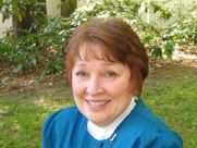 A woman in a blue shirt is smiling for the camera while sitting in the grass.