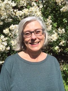 A woman with gray hair and a gray shirt is smiling for the camera.