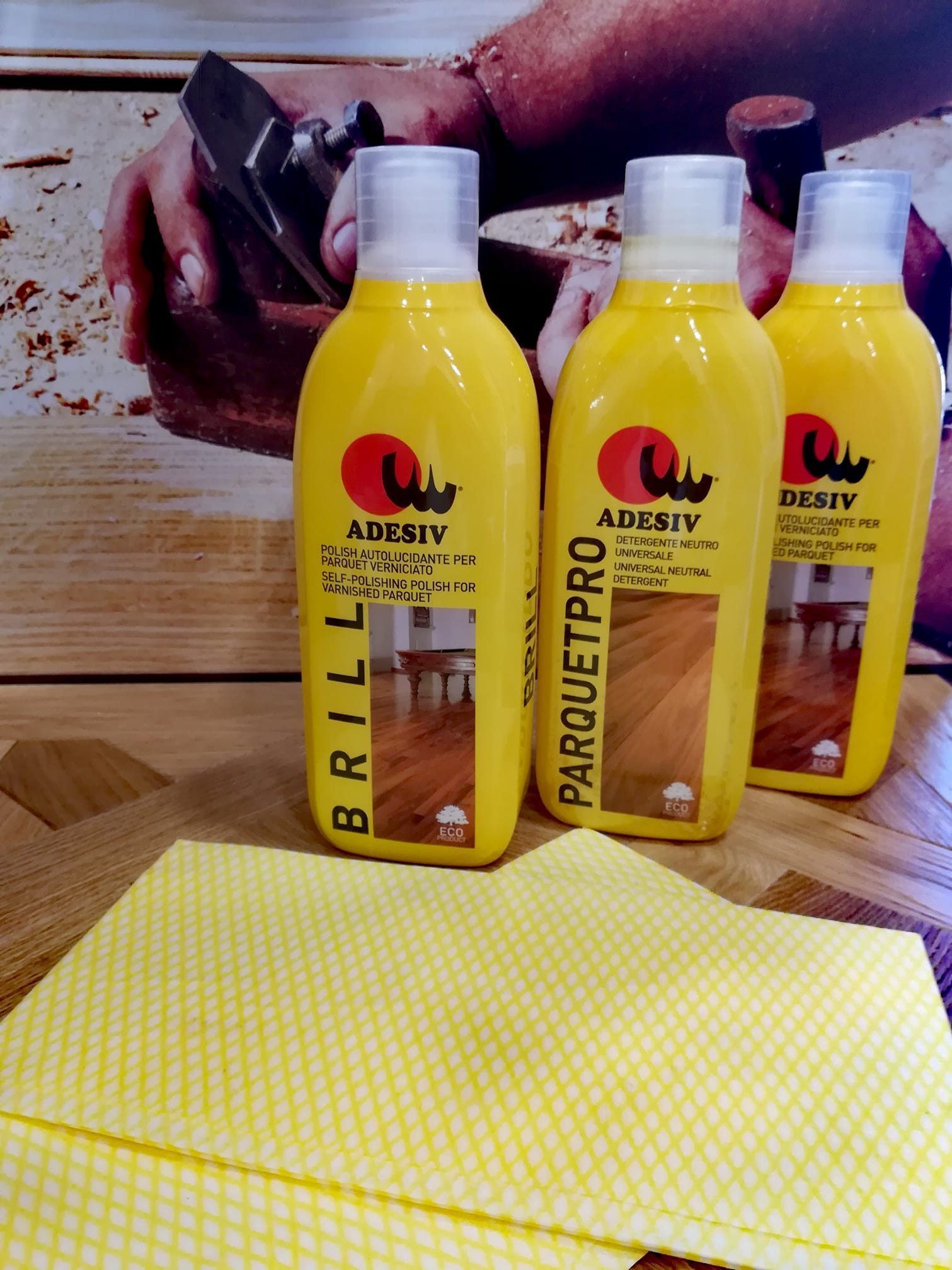 Tre bottiglie gialle di detergente per pavimenti con un panno giallo davanti.