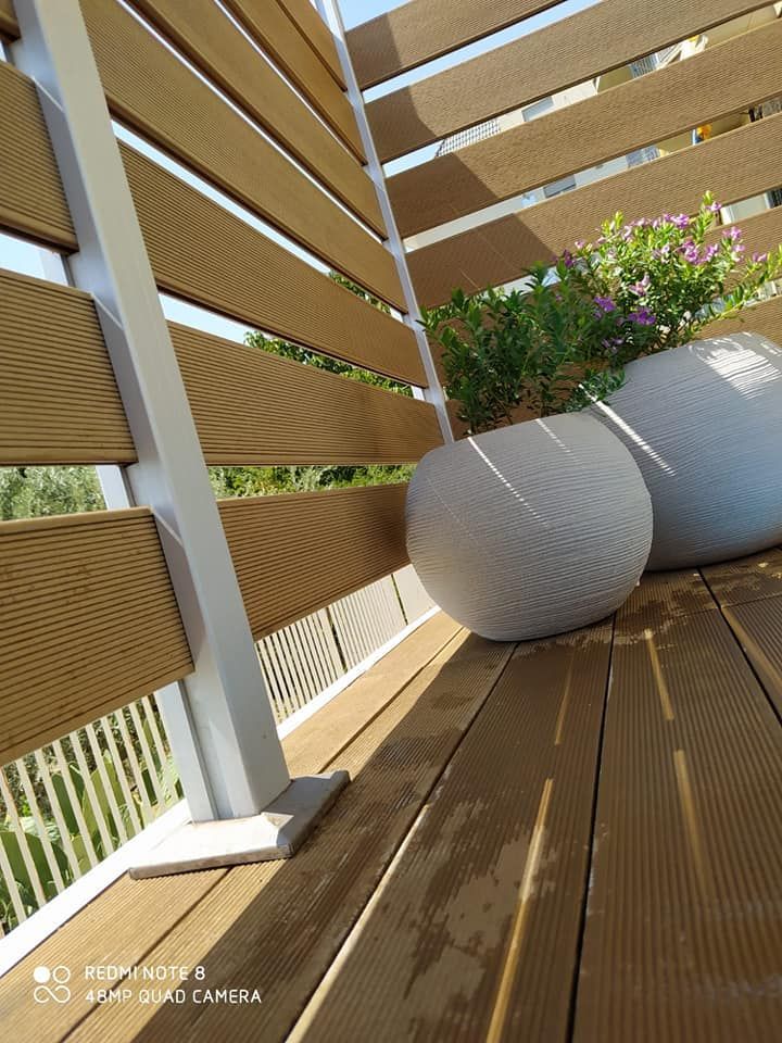 Terrazza in legno con vasi di fiori e ringhiera in legno a doghe esposta alla luce del sole.