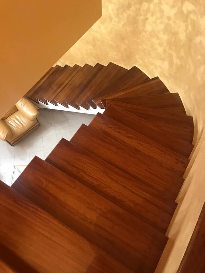 Scala a chiocciola in legno con pareti color marrone chiaro e poltrona in pelle beige.