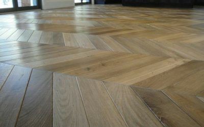 Primo piano di un pavimento in legno con motivo a chevron, con assi marrone chiaro e scuro.