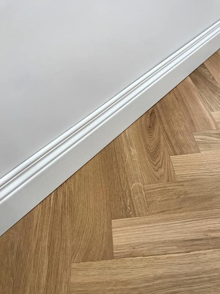 Parete e battiscopa dipinti di bianco con pavimento in parquet di rovere.