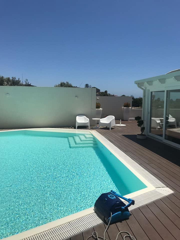 Piscina e area solarium con sedie bianche e un pulitore per piscina sotto un cielo azzurro e limpido.