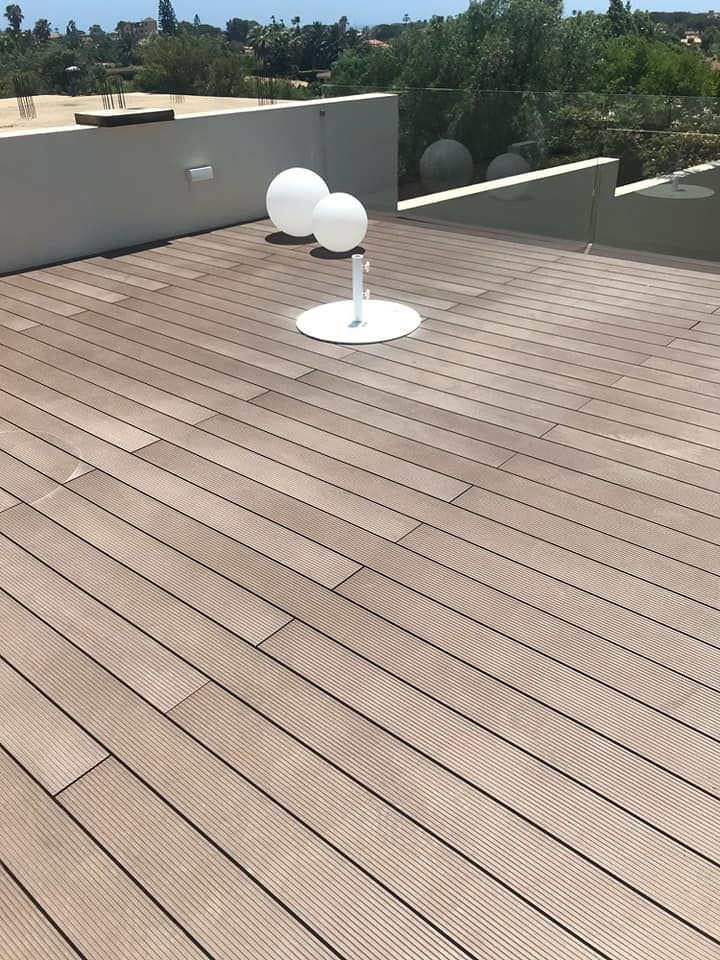 Terrazza sul tetto con assi di legno, luci a globo bianche e un muretto basso; alberi e cielo sullo sfondo.
