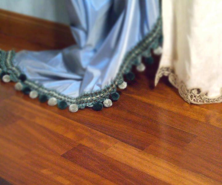 Tenda blu con pon pon verdi e bianchi su un pavimento in legno accanto a una tenda bianca.