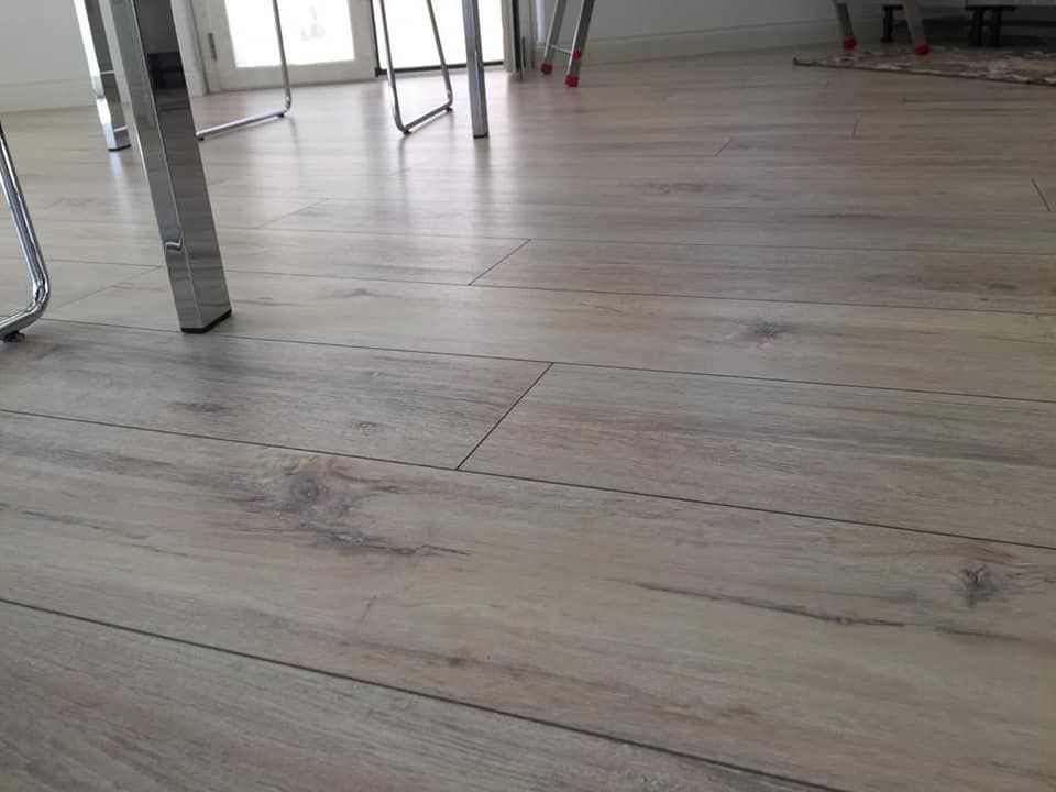Primo piano del pavimento in laminato grigio chiaro con le gambe del tavolo sullo sfondo.