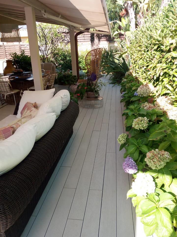 Patio esterno con pavimentazione bianca, divano scuro e aiuole con ortensie.