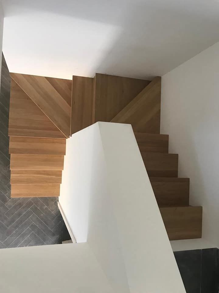 Scala in legno con motivo a chevron sul pianerottolo. Parete bianca a destra e piastrelle grigie a spina di pesce.