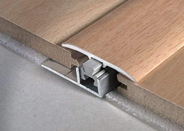 Pavimento in legno con striscia di transizione in metallo che unisce due sezioni del pavimento.