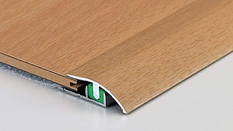 Fascia di transizione effetto legno tra due superfici del pavimento, con base in metallo e parte superiore curva.