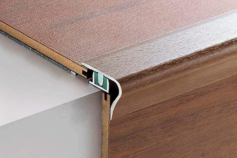 Primo piano del bordo di una scala con pavimento in legno e finiture in metallo, che mostra i dettagli dell'installazione.