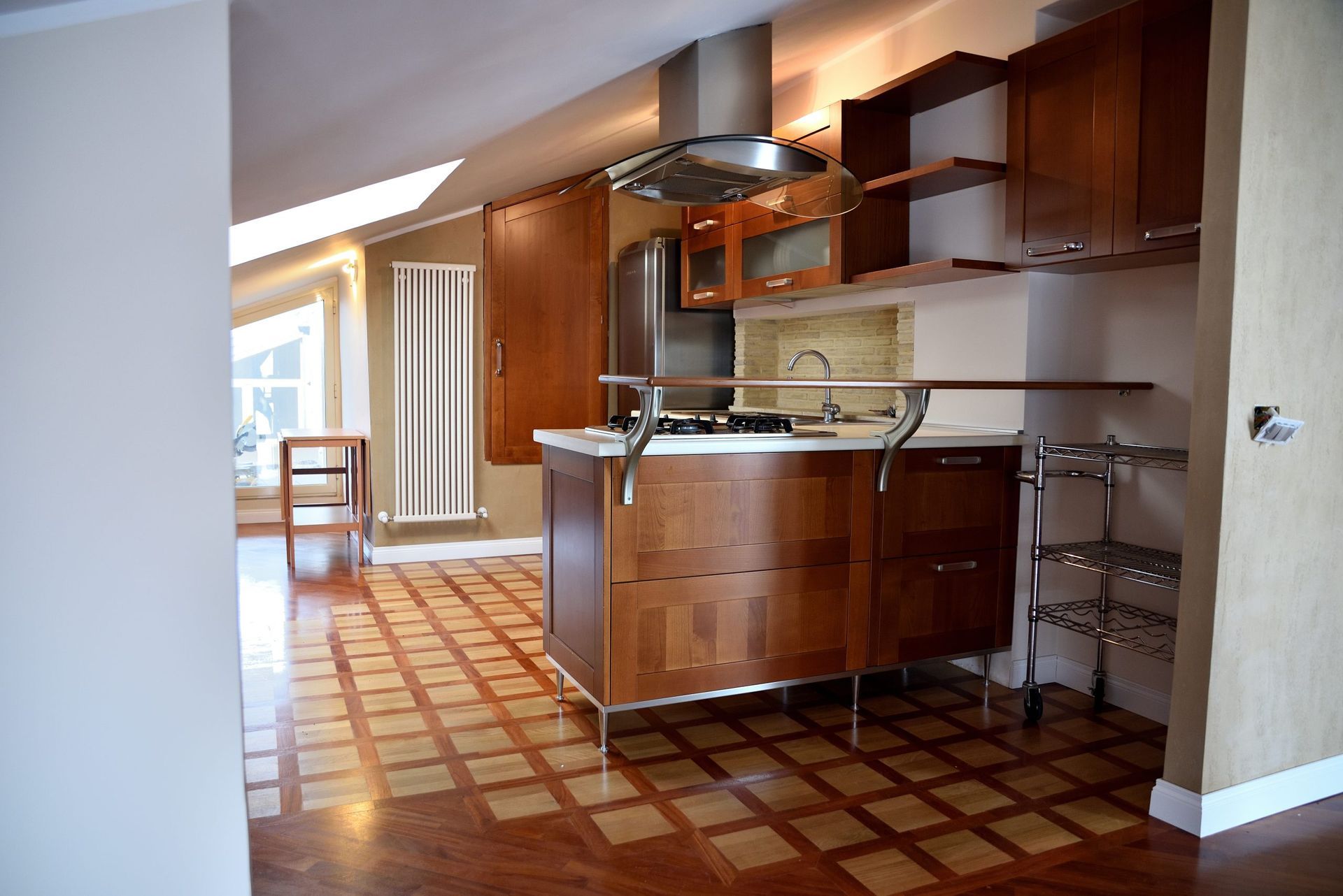 Cucina moderna con mobili in legno, isola e pavimento piastrellato; elettrodomestici da incasso.