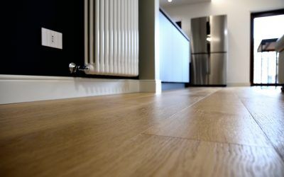Pavimento in legno all'interno, vista del radiatore contro la parete scura e frigorifero in acciaio inossidabile.