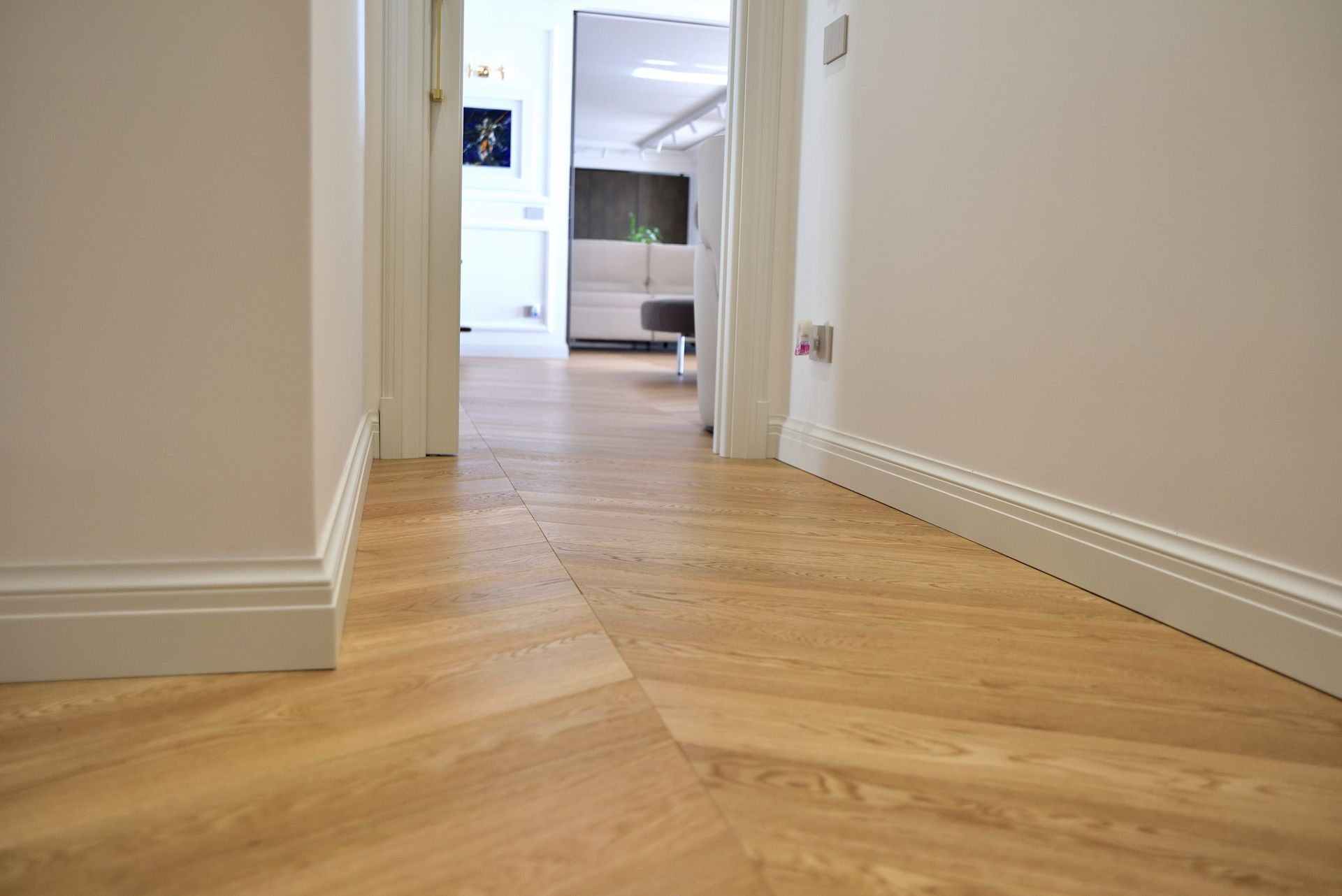 Corridoio con pavimento in legno chiaro a spina di pesce, finiture e porte bianche.