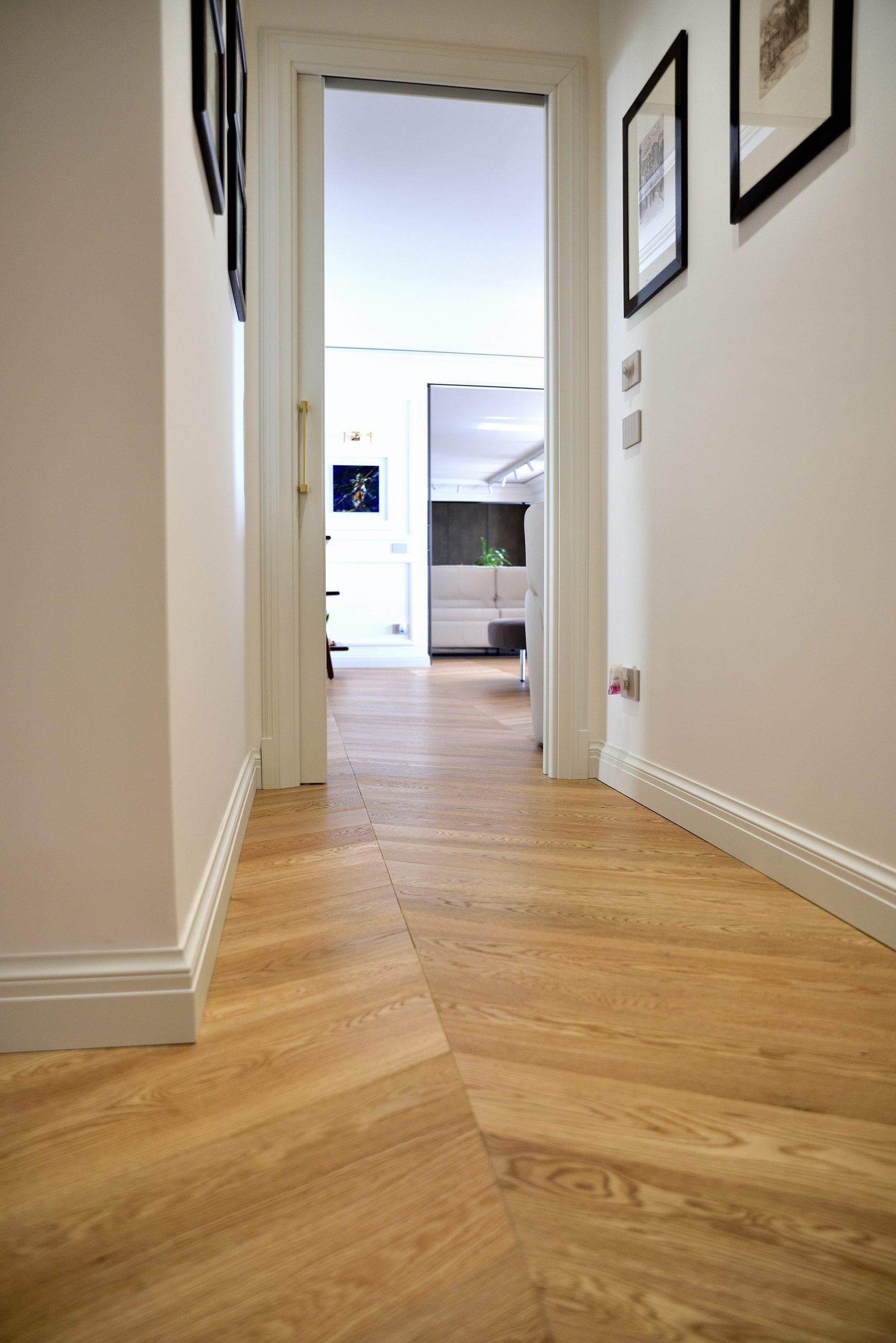 Corridoio con pavimenti in legno chiaro a spina di pesce e pareti bianche; porta in fondo.