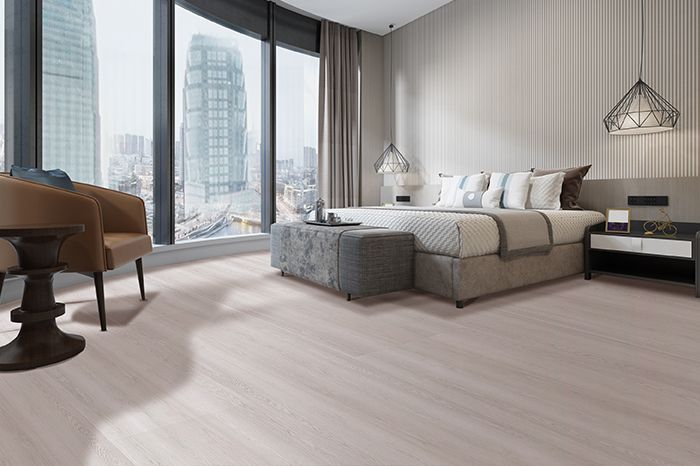 Camera da letto moderna con ampie finestre, vista sulla città, letto, poltrona e pavimento in legno chiaro.
