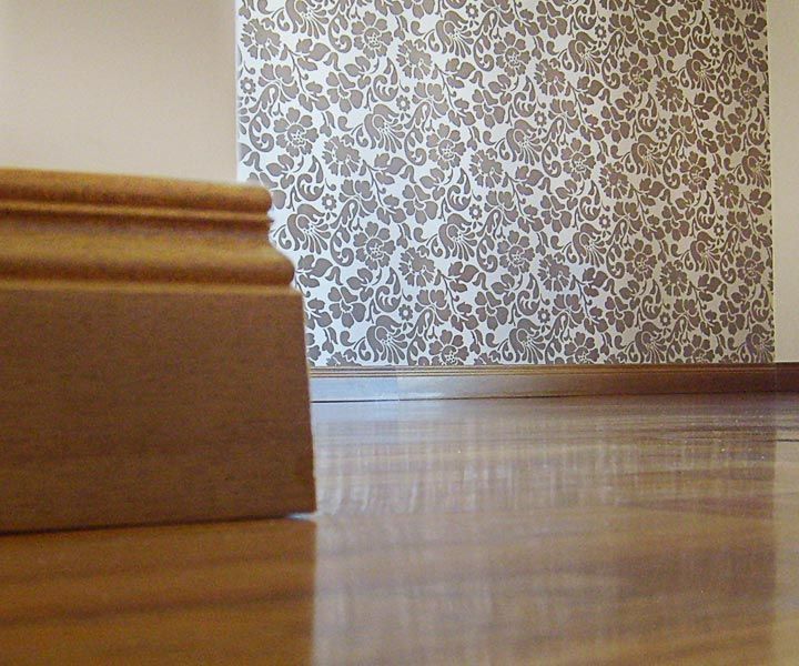 Battiscopa e pavimento in legno con carta da parati floreale sullo sfondo.
