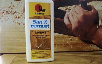 Flacone di colla per parquet ADESIV San-X, con una scena di lavorazione del legno sullo sfondo.